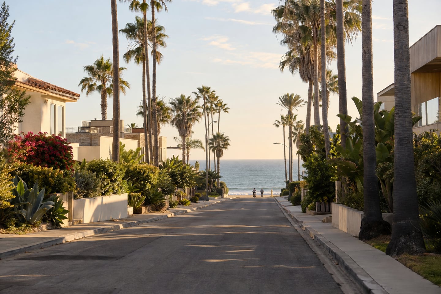 A quiet beach-town street with palm trees and the ocean in the distance.