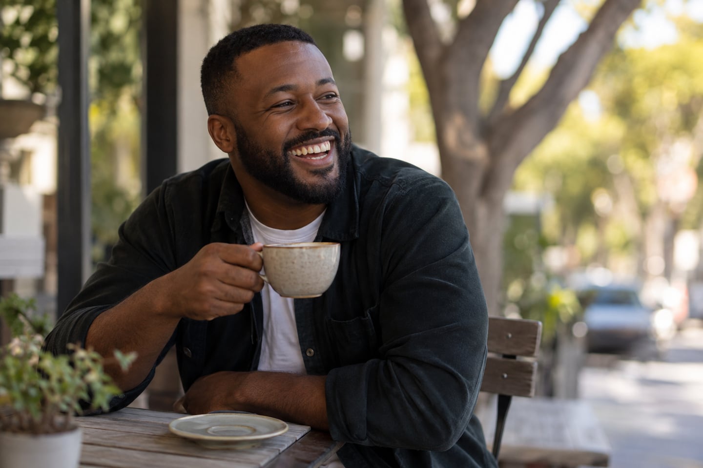An adult laughing over a cup of coffee at an outdoor café.