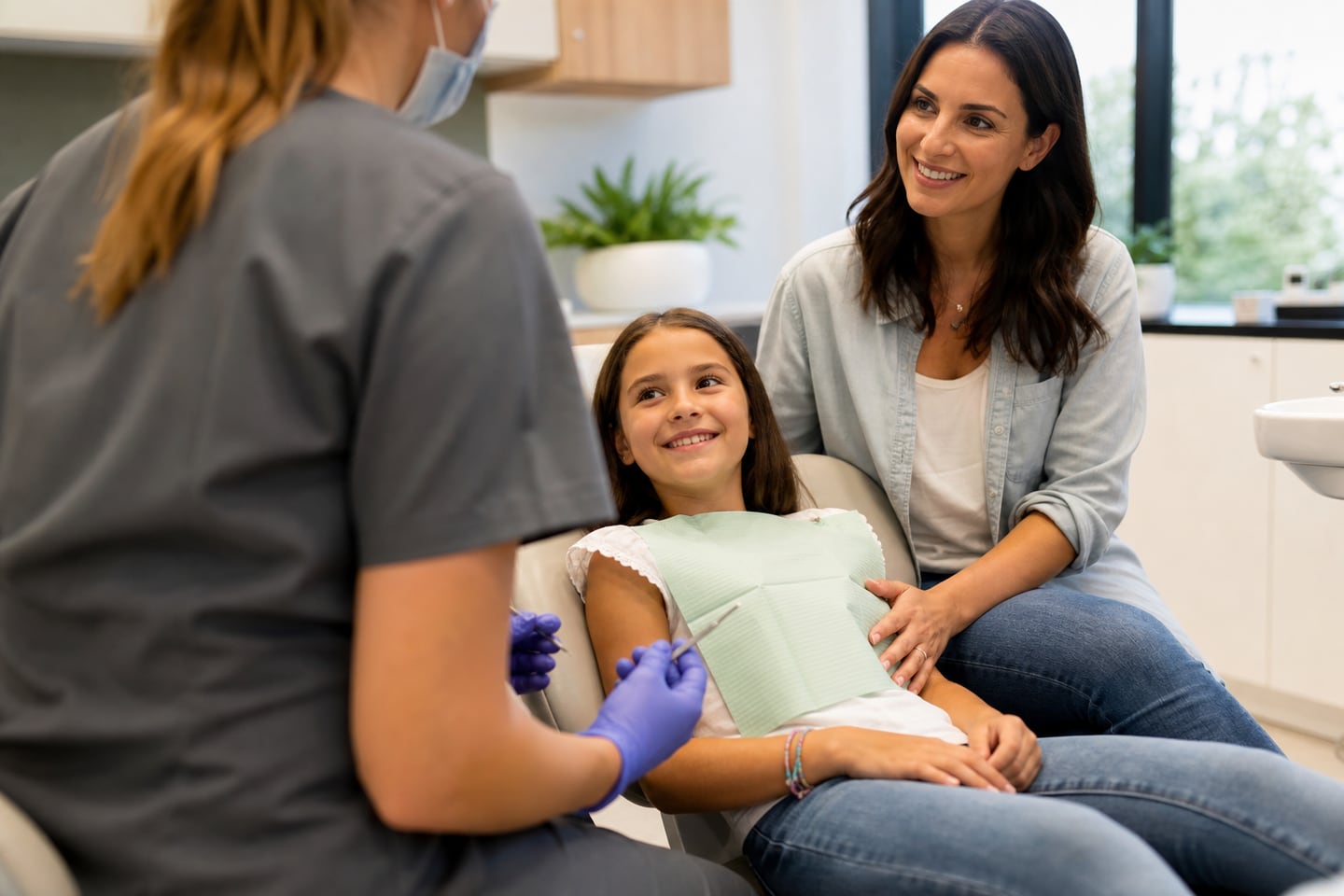 A dentist talking with a young child at eye level while a parent sits beside them.